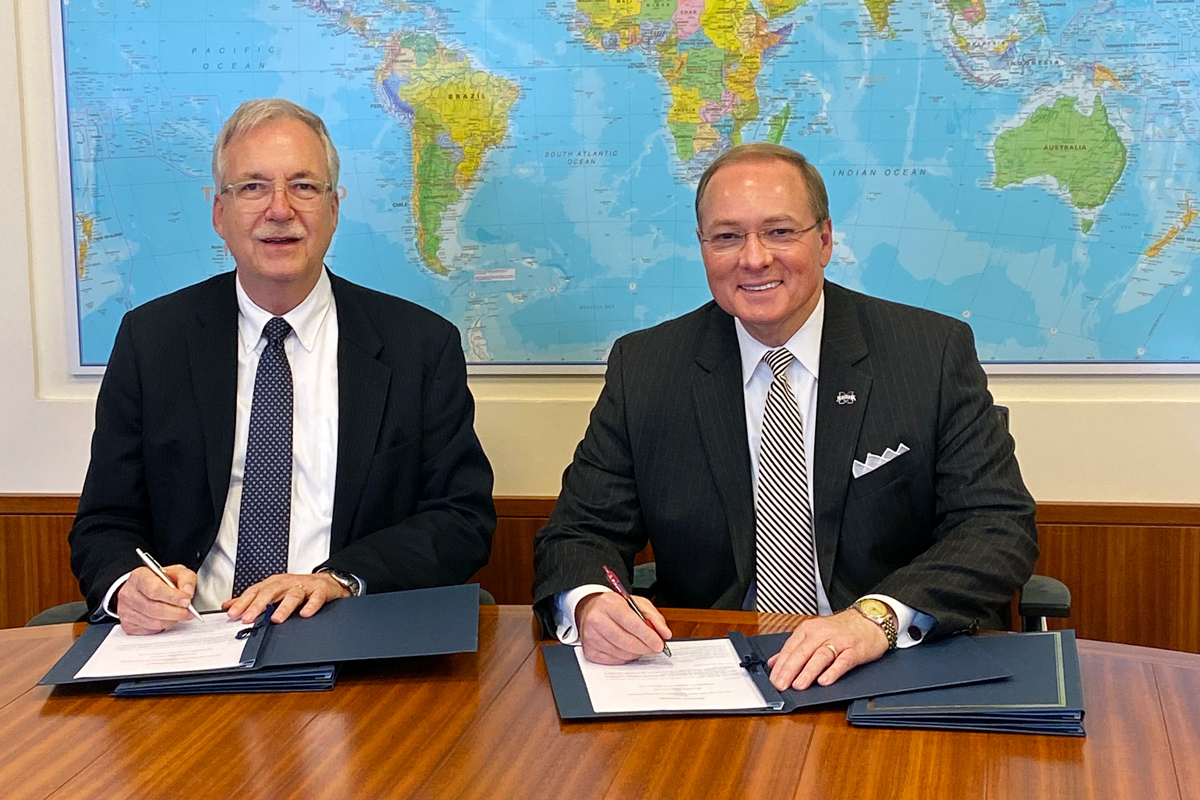 With a map behind them, UN FAO Deputy Director-General for Programmes Daniel Gustafson and President Keenum sign MOUs.