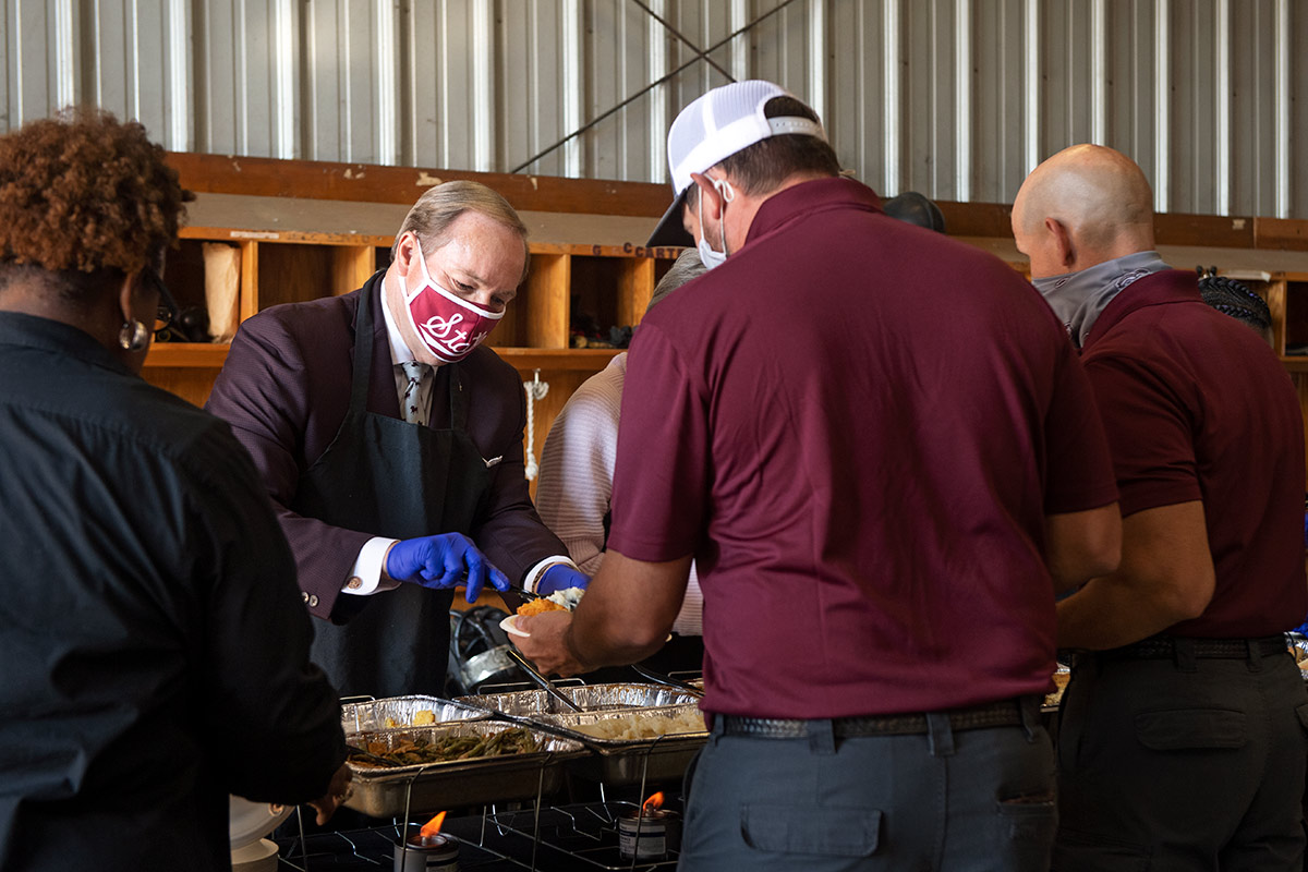 Man in maroon blazer and mask serving food to man in maroon shirt at fire station