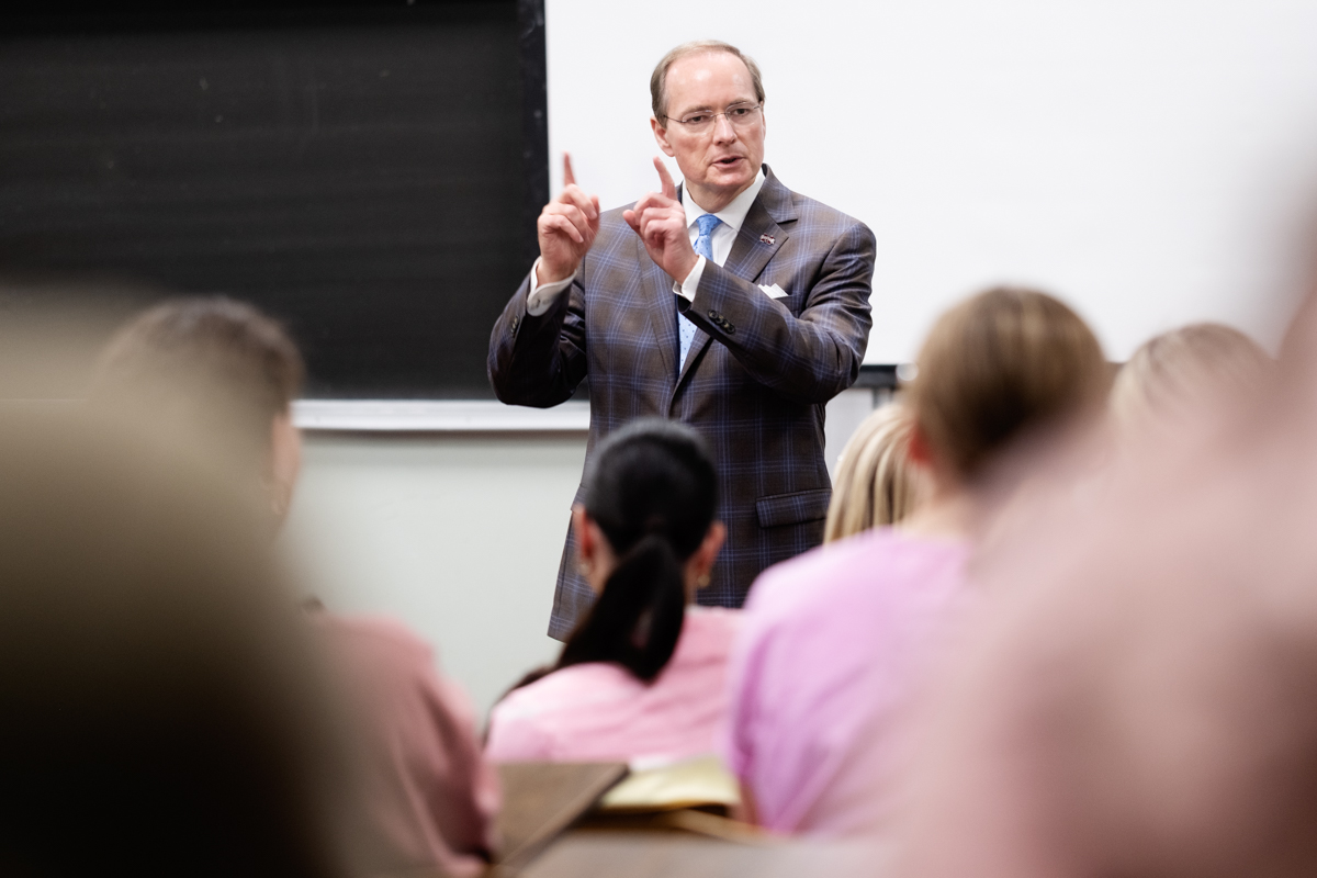 With the blurry backs of attending Maroon VIP students framing him, President Keenum speaks towards the camera.