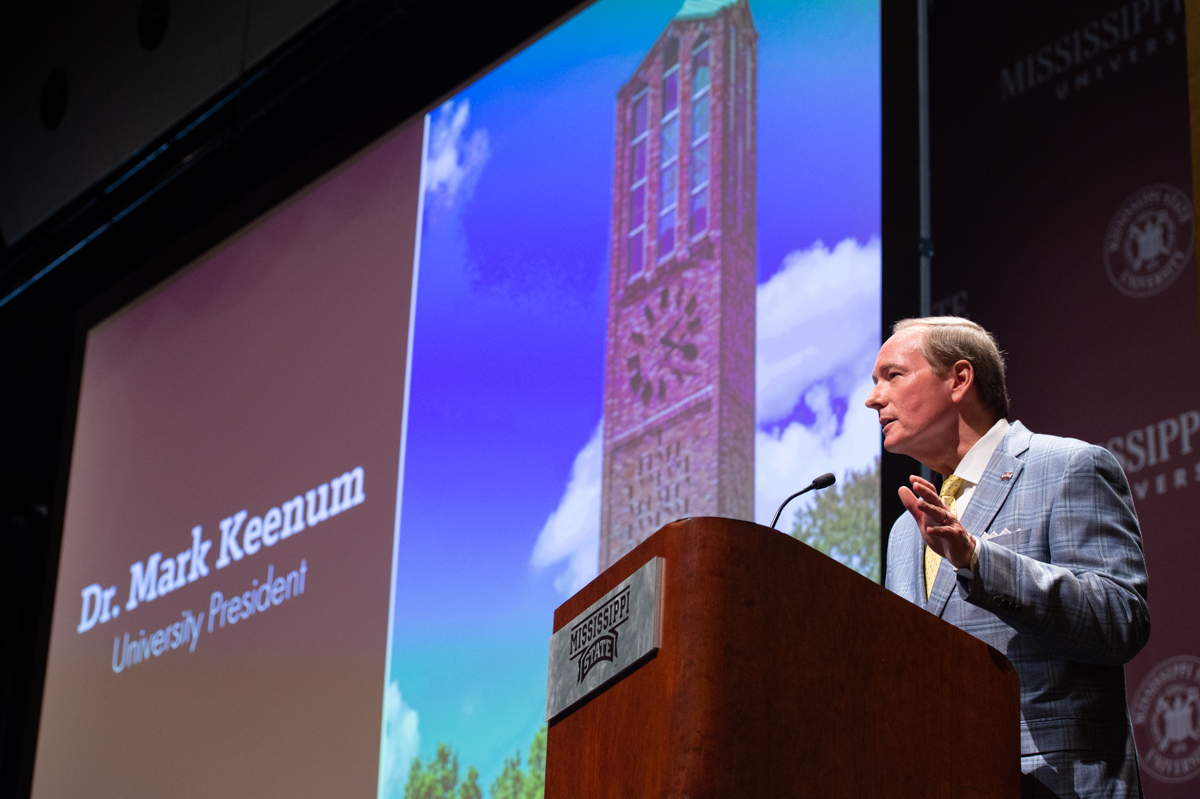 President Keenum speaks from the Bettersworth Audiorium podium with a screen behind showing a photo of the Chapel Tower.
