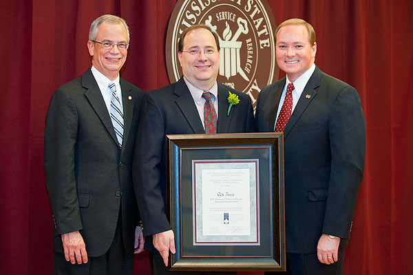 Jerry Gilbert, MSU provost and executive vice present, left, and university President Mark E. Keenum, congratulate associate professor of political science and public administration Rick Travis during a ceremony in Mitchell Memorial Library's John Grisha