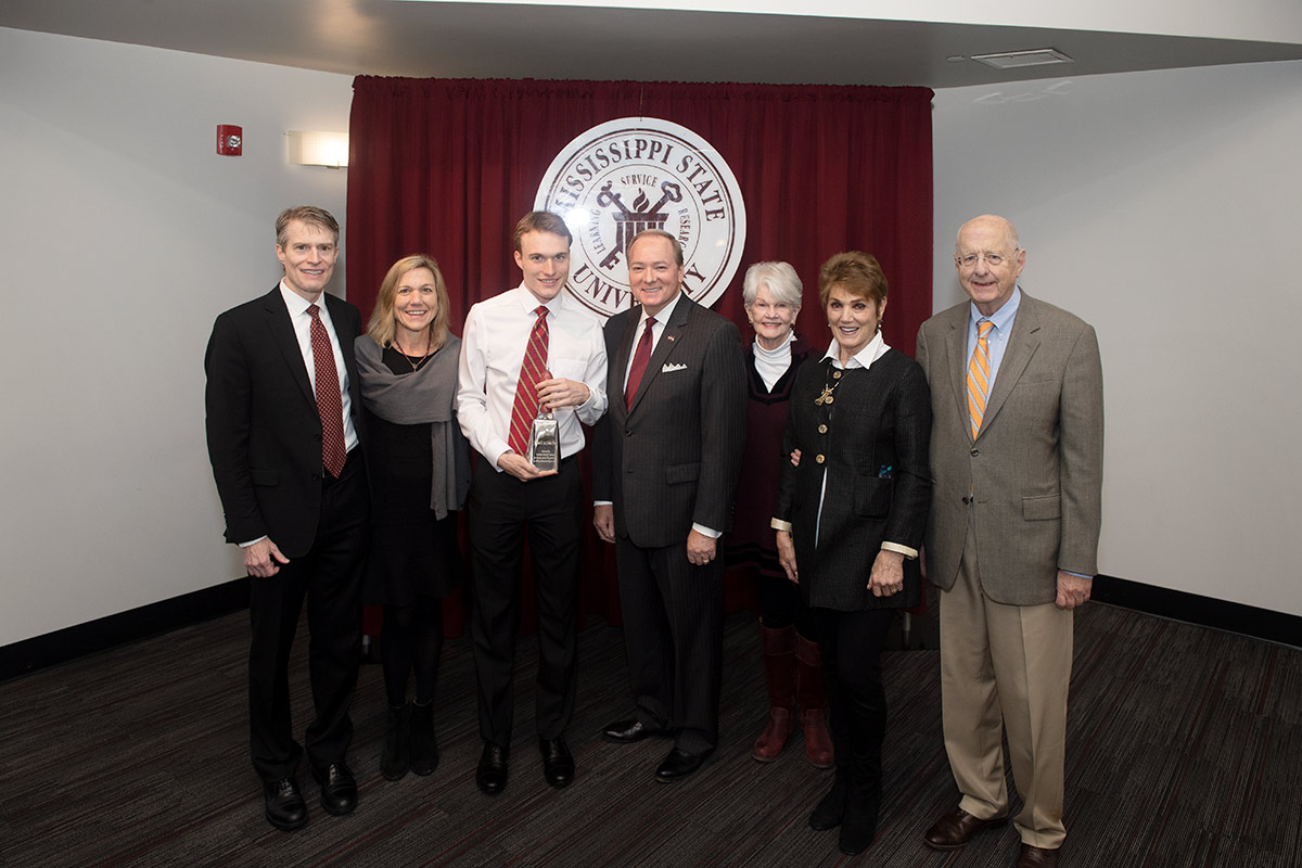 Group of well dressed people in front of maroon drapery with MSU seal