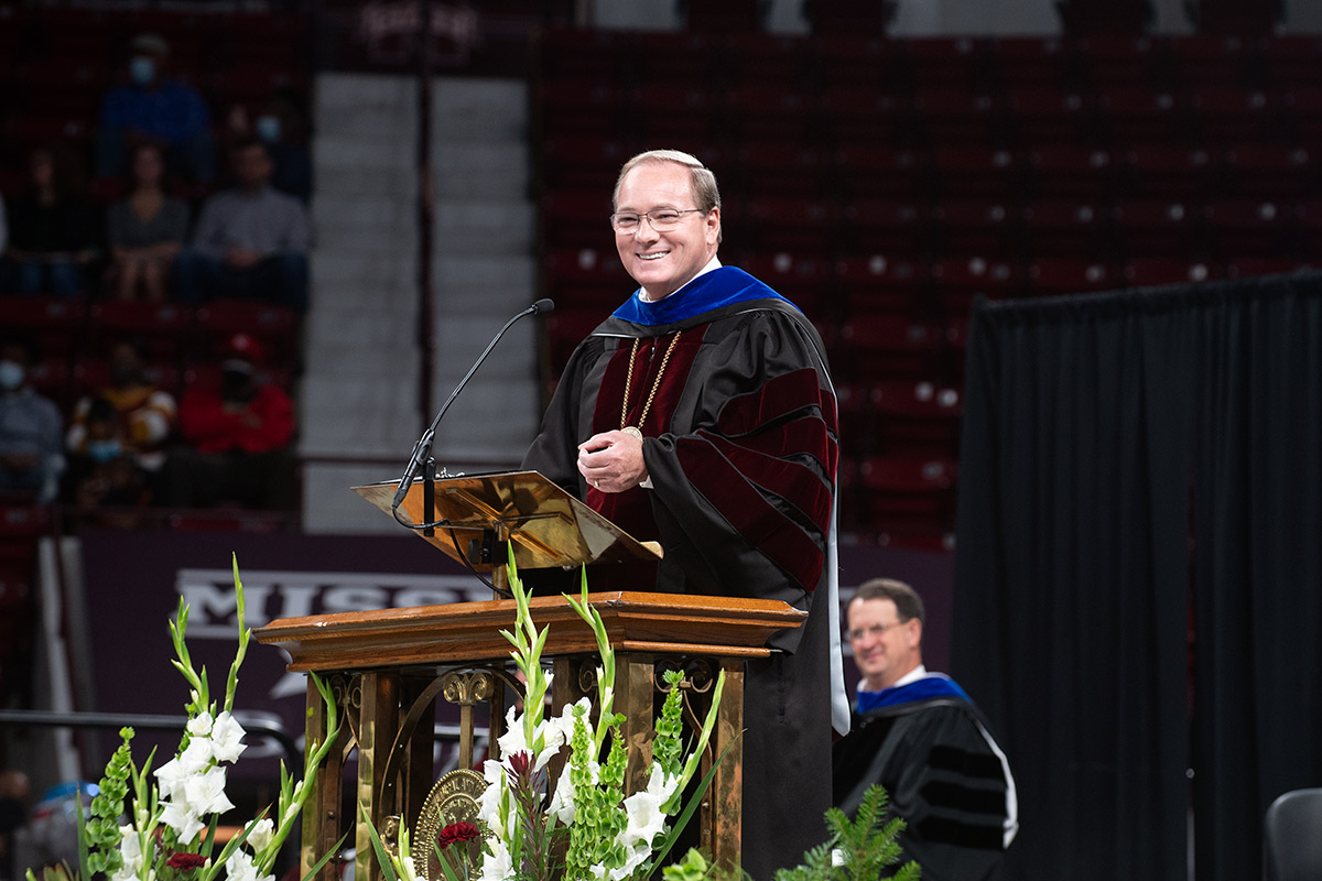 Man in graduation regalia speaking at podium