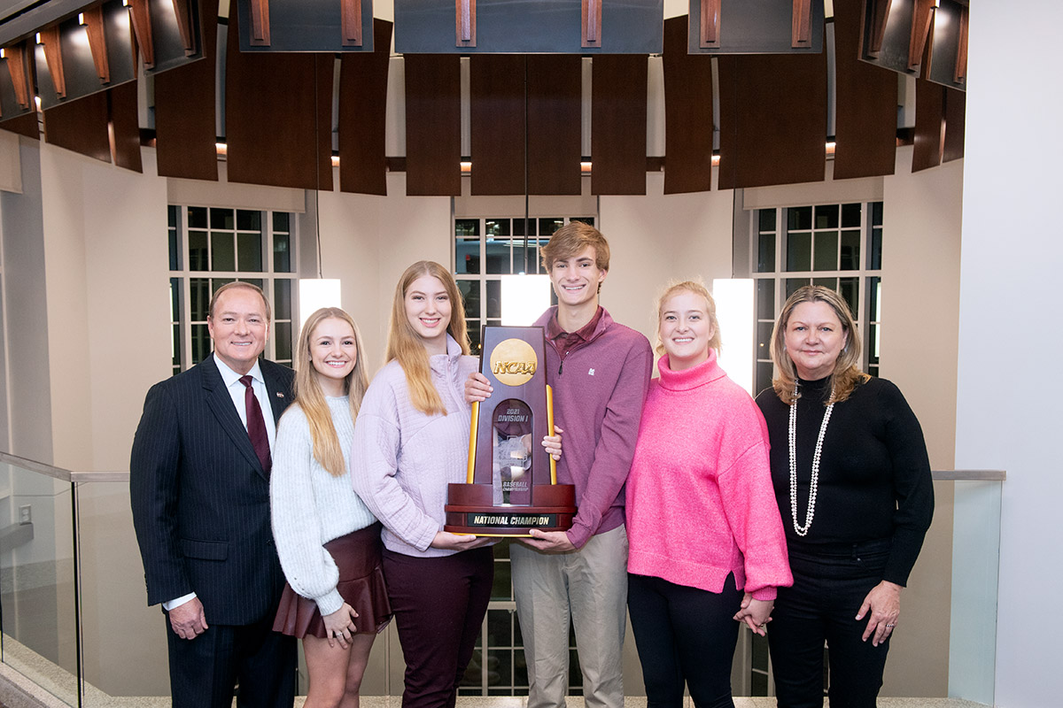 Family posed near railing and holding a large trophy with an atrium in the background