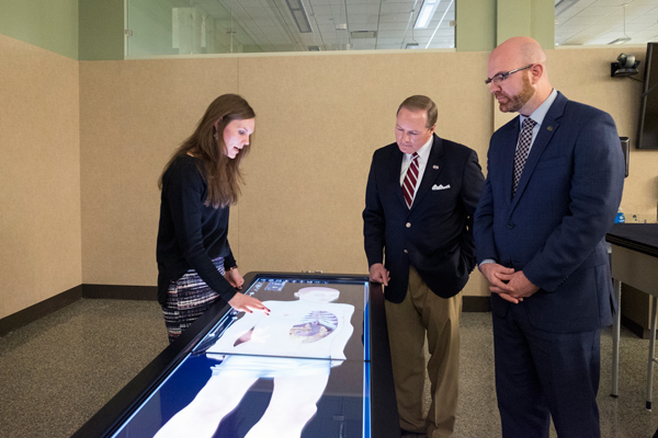 Mississippi State University-Meridian interim Kinesiology program coordinator and director of the Clinical Exercise Physiology Labs Laura Hilton, left, demonstrates the Anatomage virtual dissection table to MSU President Mark E. Keenum, center, and MSU-M