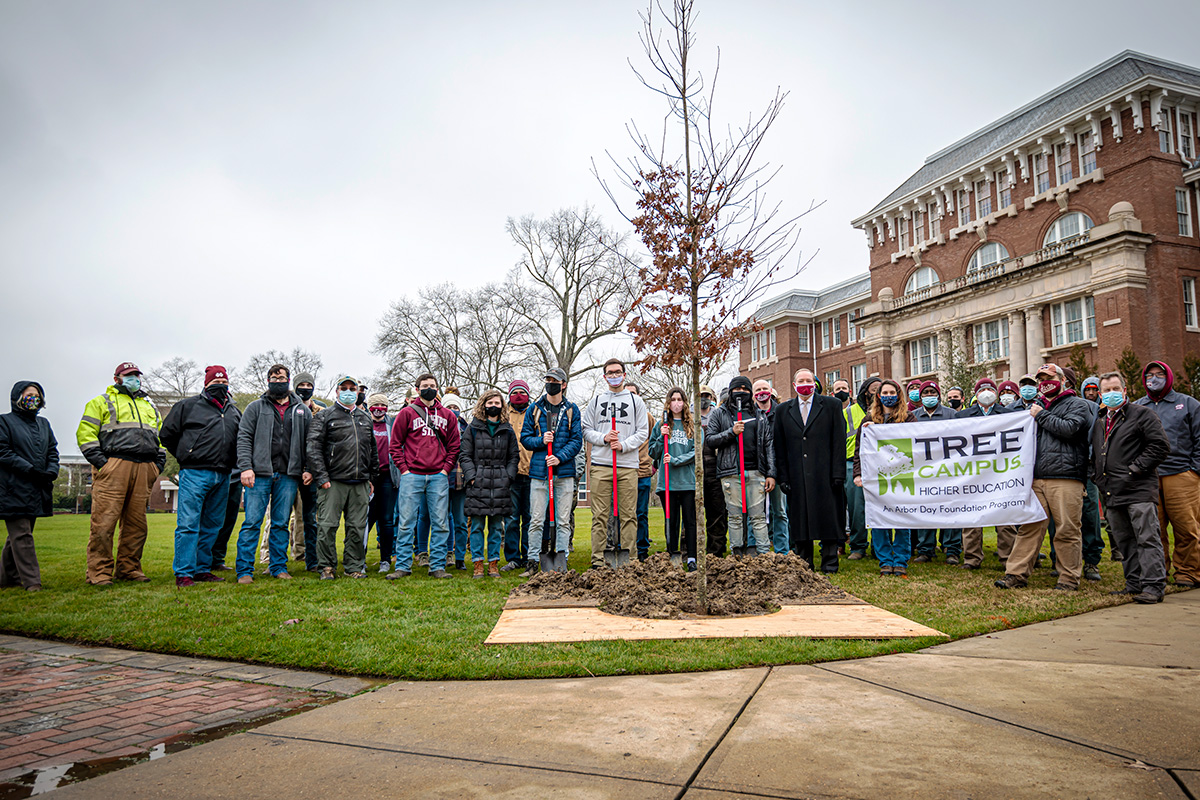 President Keenum joins a group of CFR people and campus landscape personnel, standing with a newly planted tree.