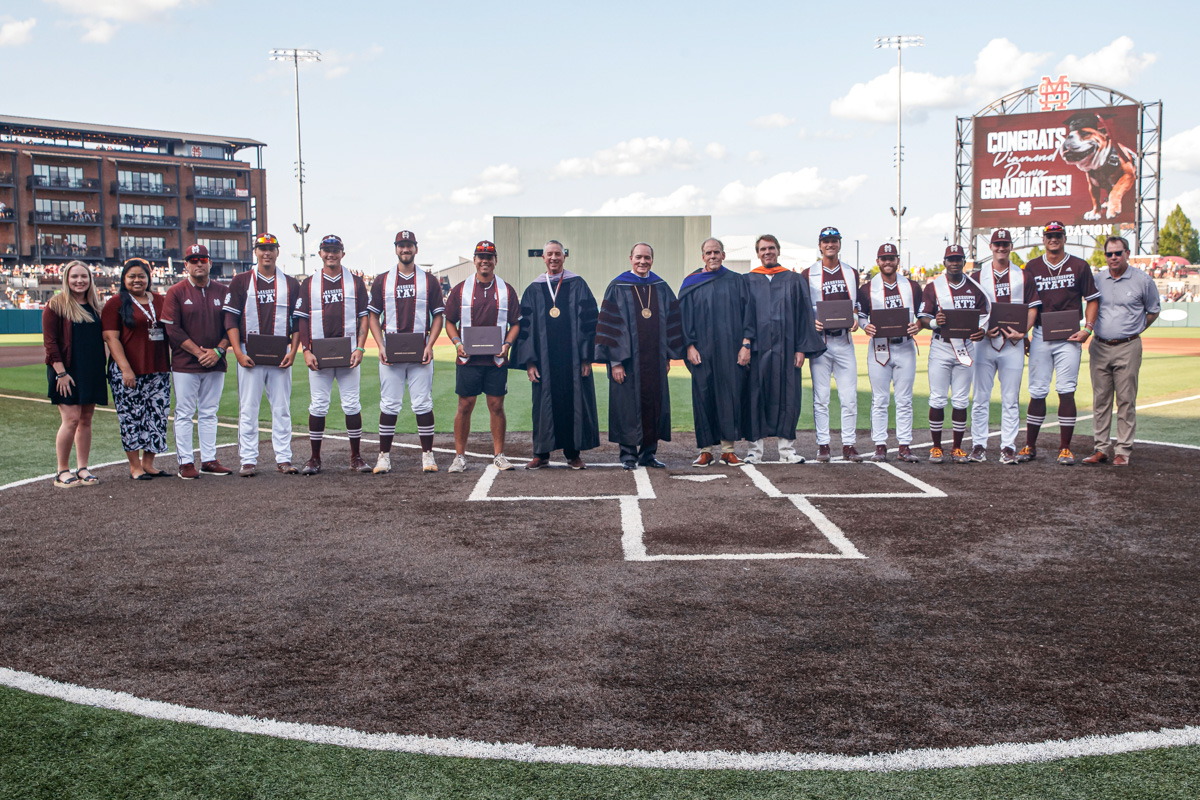 President Keenum and IHL Board Members wear full reglaia on Dudy Noble Field whle posing with graduating Baseball team members.
