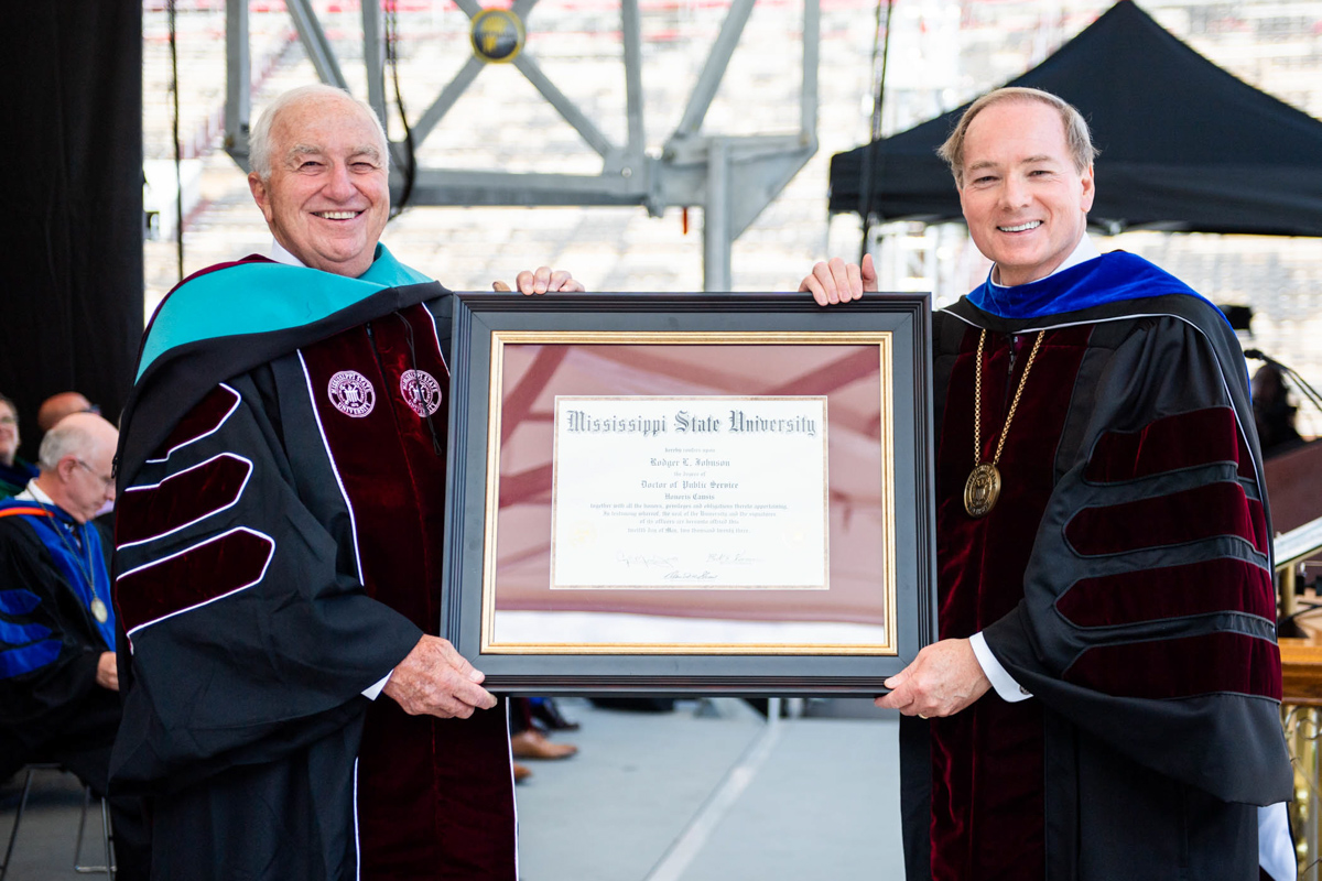President Keenum (right) and Rodger L. Johnson stand on the graduation platform, holding Johnson's framed honorary Doctorate.