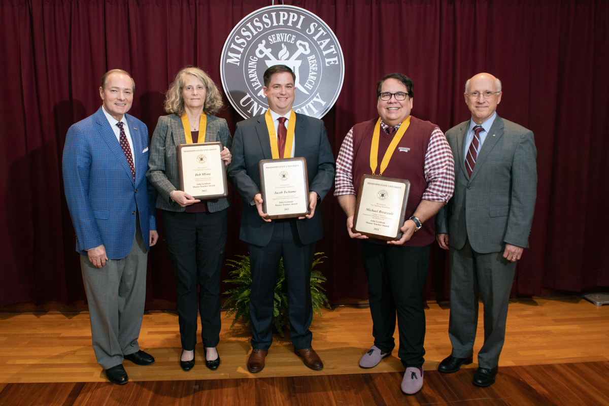 The three Grisham Master Teachers for 2022 stand in front of the MSU seal and pipe and drape, bookended by Keenum and Shaw