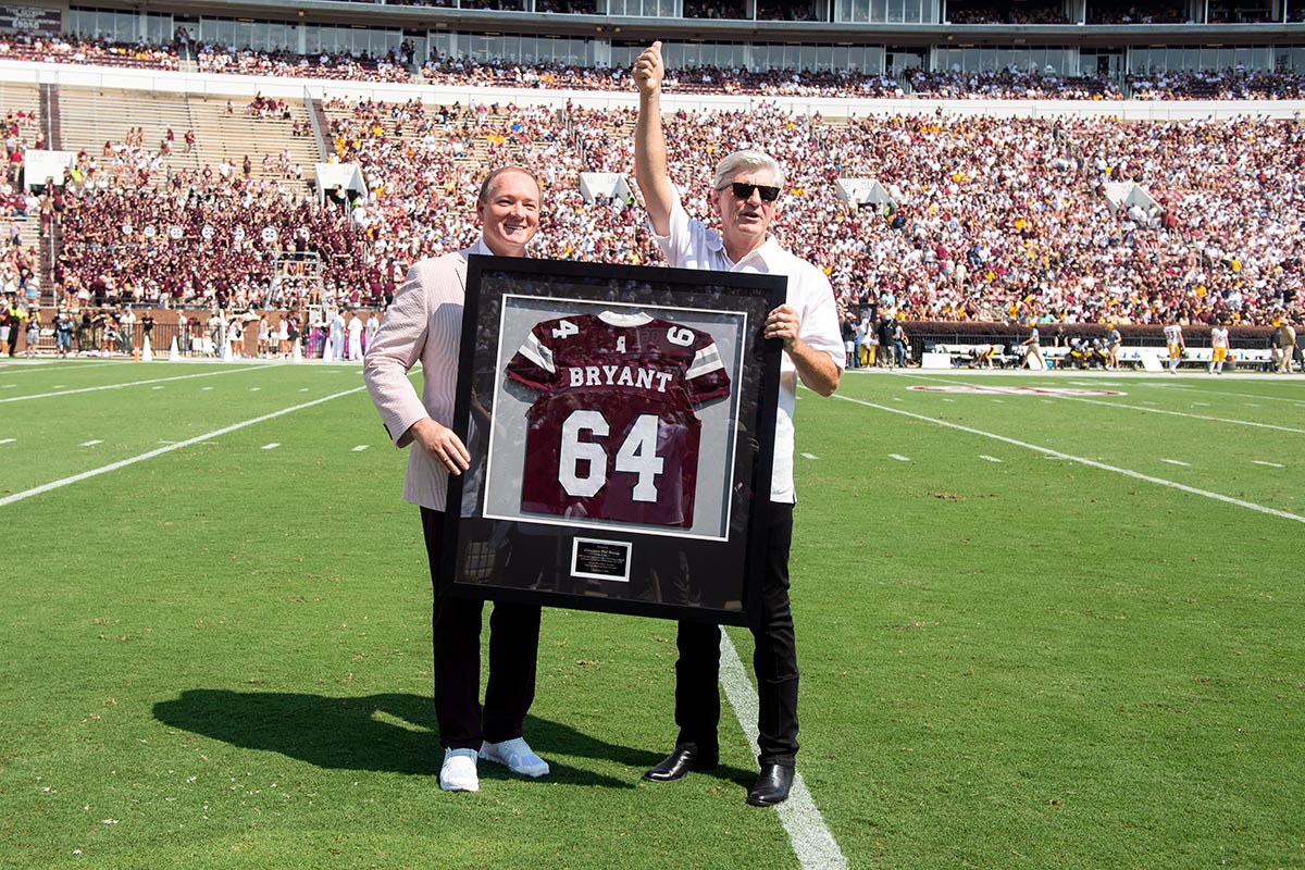 Two men on football field with framed jersey