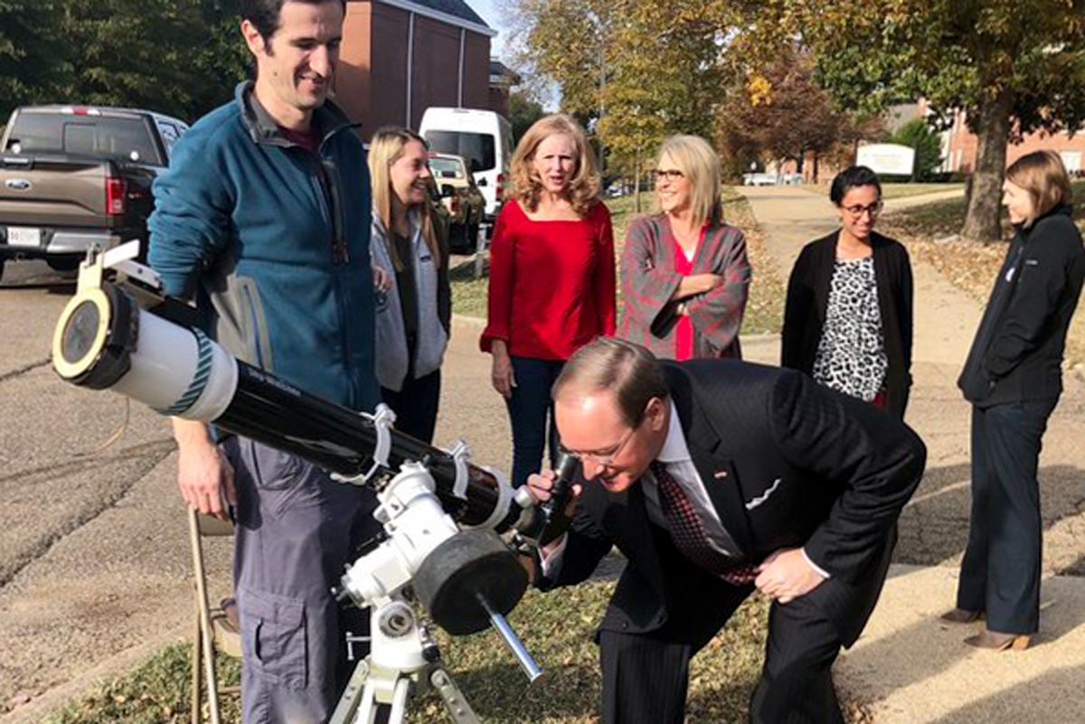 Surrounded by other MSU staff members, President Keenum bends to look through a telescope at the transit of Mercury.