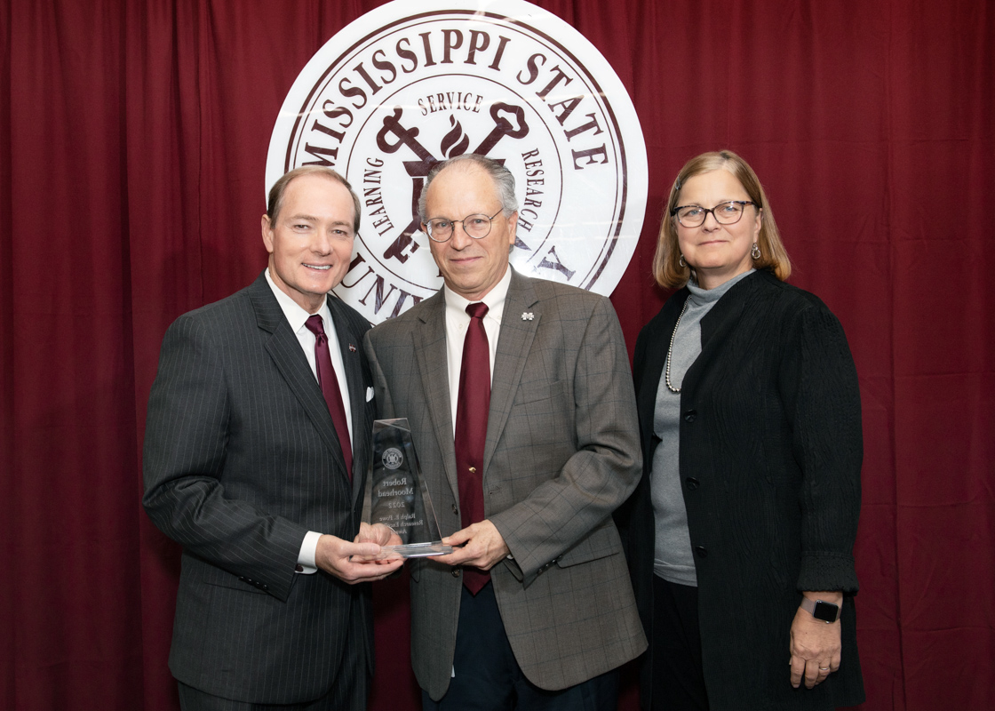 President Keenum and VP Jordan frame Dr. Moorhead, who holds his glass Powe Award in front of the MSU Seal.
