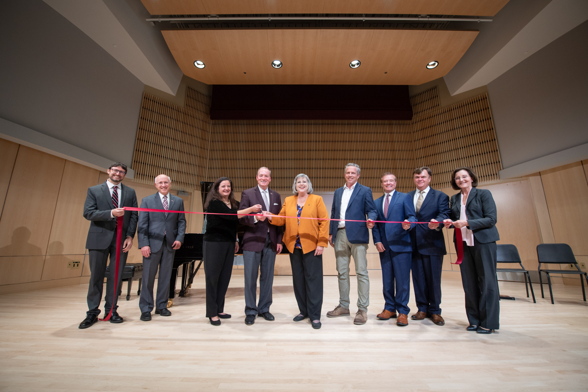 The nine participants in the Music Building ribbon-cutting smile behind the ribbon on the stage.
