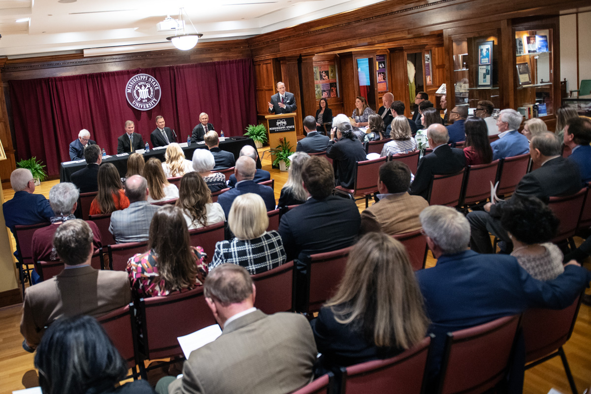 President Keenum speaks from the podium in the Grisham room, with attendees filling all the chairs in the foreground.