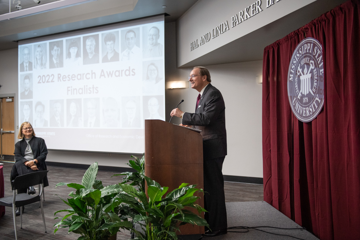 President Keenum speaks at the podium, with a slide reading "2022 Research Awards Finalists" beyond him.