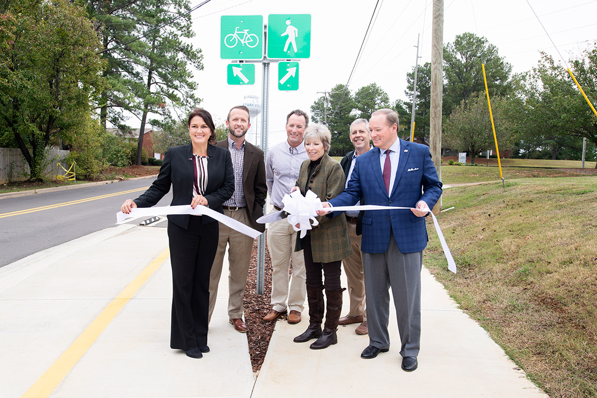 Group of people on merging pathways holding ribbon for ribbon cutting