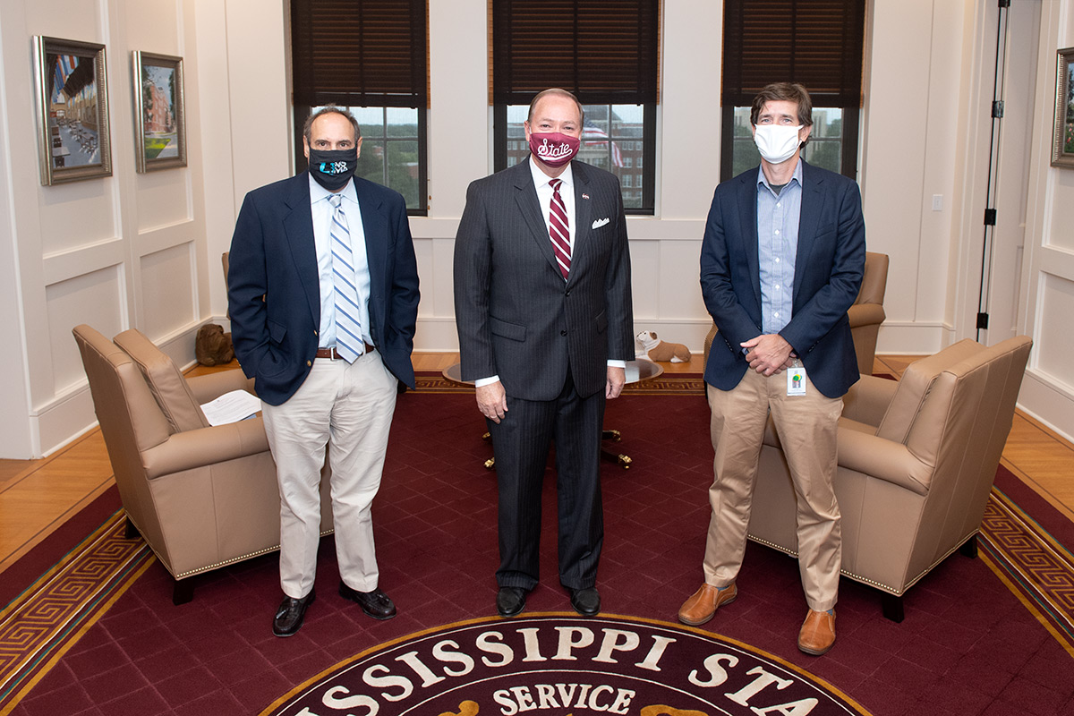 Three men in suit and tie with face coverings on standing in office setting