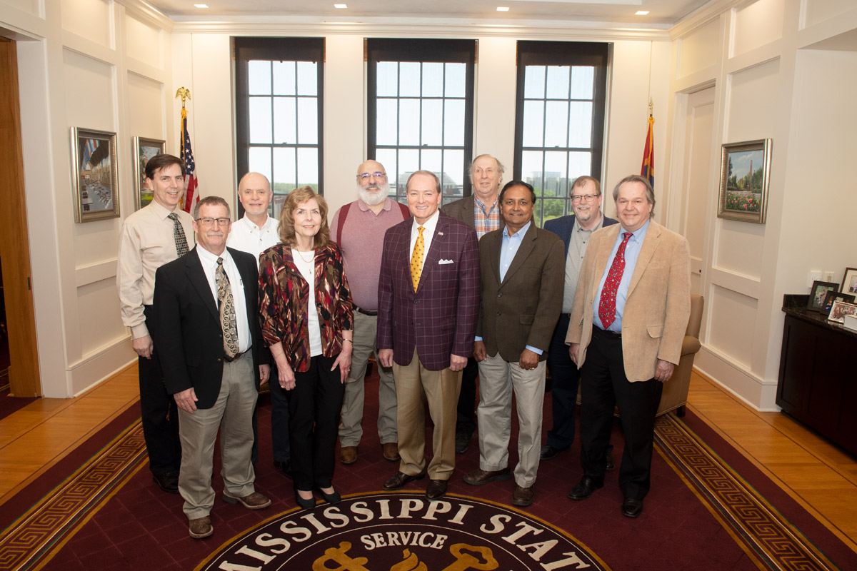 Group posed around rug with Mississippi State seal on floor