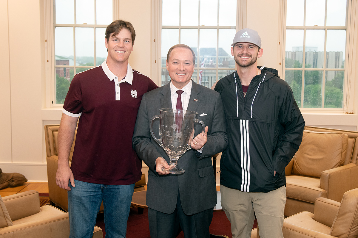 Three men standing in office with clear glass trophy