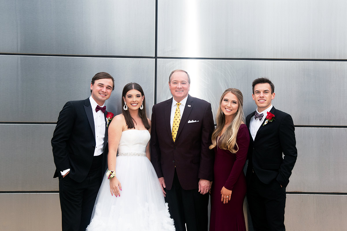 Men in suits with ladies in formal dresses near shiny wall
