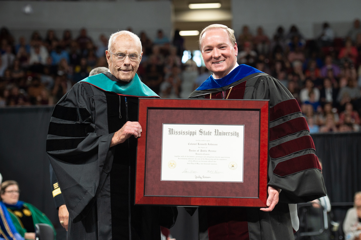 Alumni Kenneth Johnson poses for a photo, holding his honorary degree with President Keenum on the Commencement stage.