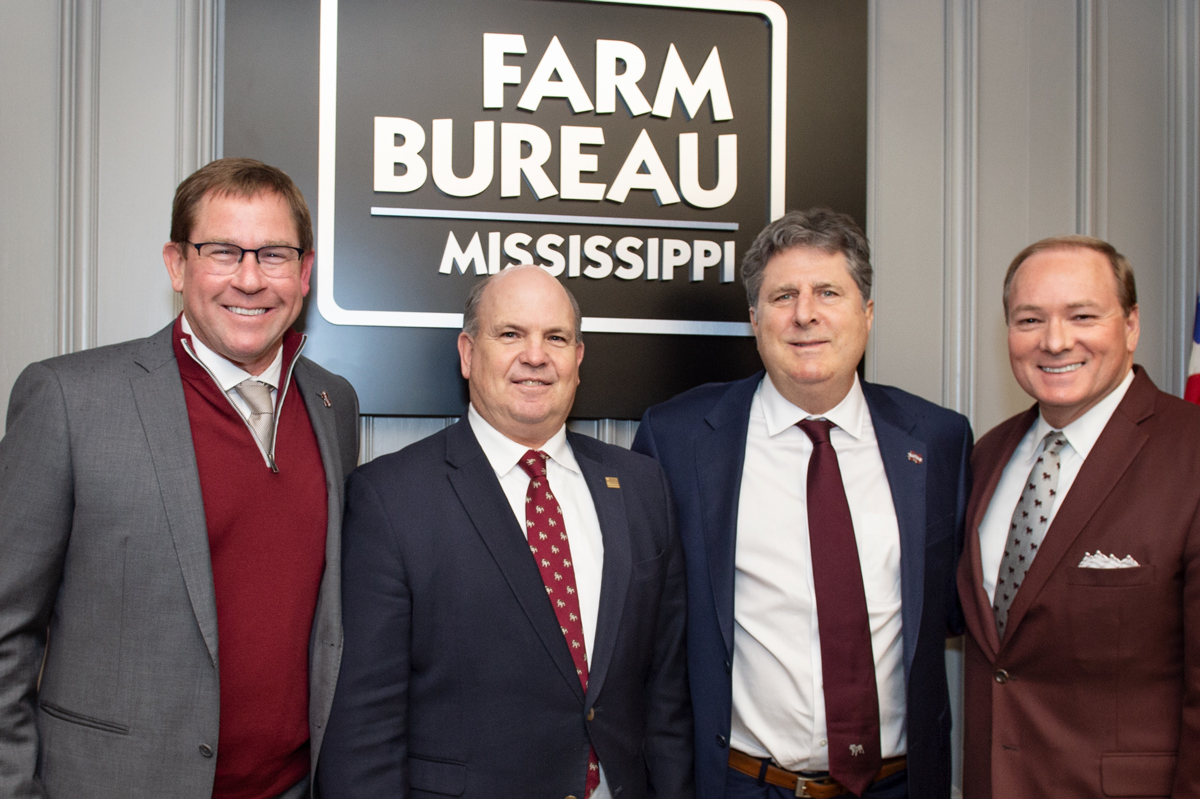 John Cohen, Mike McCormick, Coach Leach, and President Keenum pose in front of Farm Bureau sign.