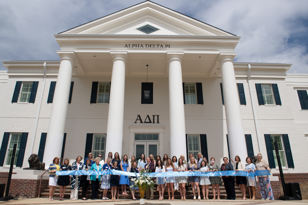 President Keenum stands in front of the new Alpha Delta Pi sorority house, posed holding the ribbon with dozens of ADPi women.
