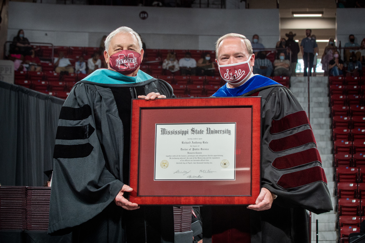 Engineering alum Richard Rula and President Keenum hold Rula's framed honorary degree between them, wearing graduation regalia.