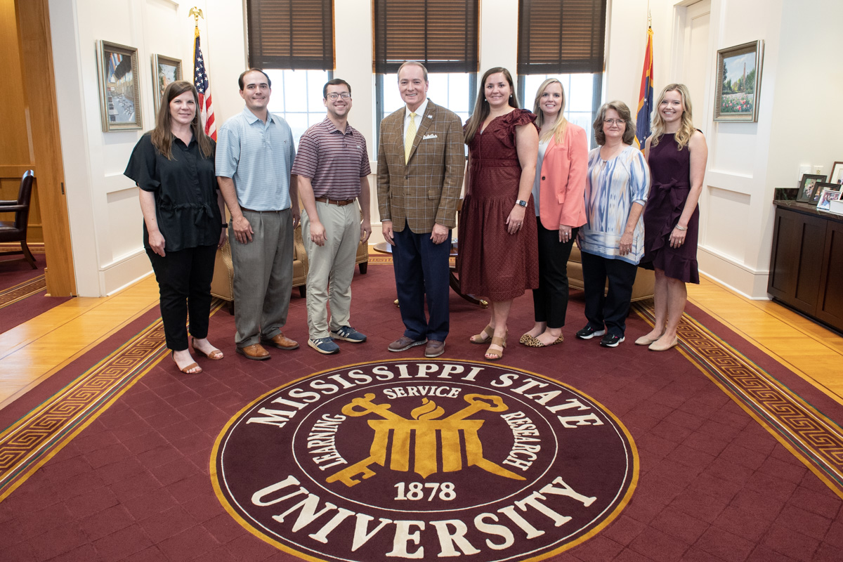 President Keenum poses at the MSU seal carpet with Staff members representing Mississippi Lt. Gov. Delbert Hosemann's office.