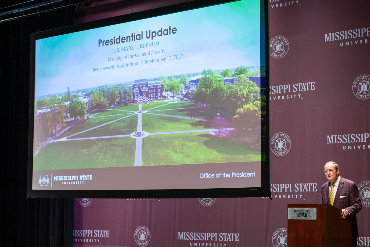 President Keenum speaks from a podium at the bottom right, with a slide of the Drill Field on a big screen.