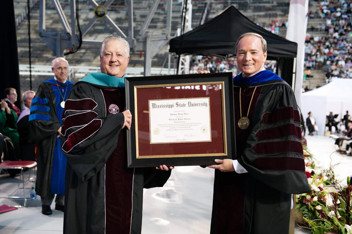 Tommy Nusz (L) and President Keenum stand on the graduation platform, holding Johnson's framed honorary Doctorate between them.